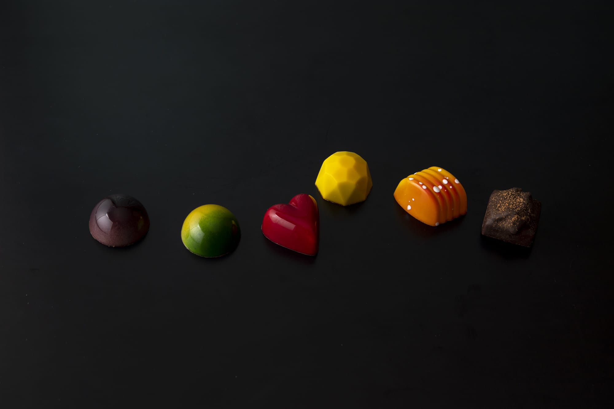 ベルギーのチョコレートは、モールド（型）を使ったものが主流。中にはフレッシュ感のあるガナッシュが詰められている。左から、ブルーベリー＆カシスの「ヴィオレ」、「ライムジンジャー」、「フランボワーズ」、「パッション」、「オレンジ」、ベルギーを代表するスパイスクッキーを入れた「スペキュロス・プリュノー」。各223円（税別）