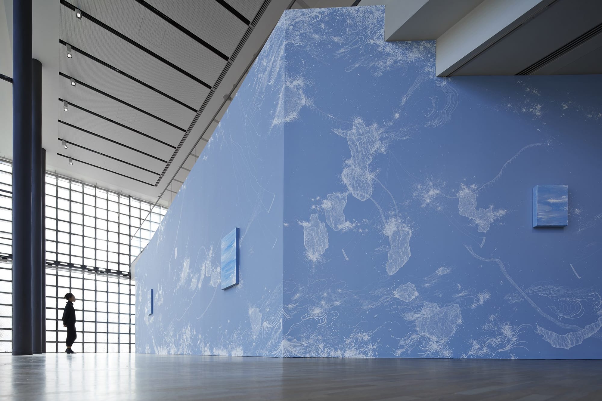 壁一面に広がる宇宙を象徴的に表すブルーをベースとして、繊細なラインで波などのモチーフが描き出されている。  展示風景/ Installation viewコズミック・ガーデン| 2020 | マーカー、アクリル、ペンキ、カンヴァス、木パネル、カーペット、スピーカー Cosmic Garden | 2020 | Permanent pen, acrylic, paint, wood panel, carpet, speaker ©Nacása & Partners Inc. / Courtesy of Fondation d’entreprise Hermès