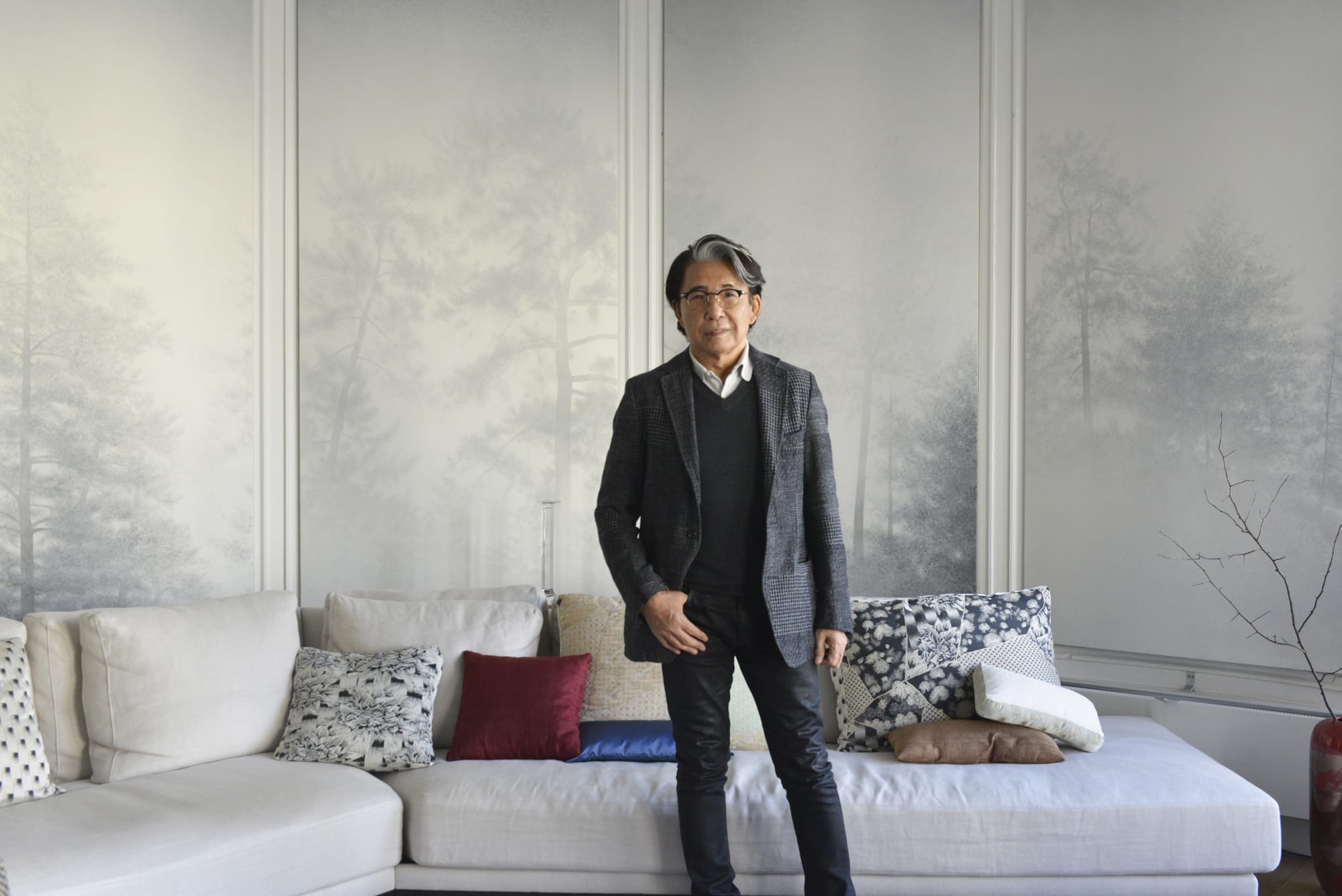アトリエでの髙田賢三。長年愛用しているソファに自身のホーム＆ライフスタイルコレクション「K三」の「Shogun」のクッションが加わった。アトリエの壁を飾るのは、パリ在住の日本画家・釘町彰の作品。