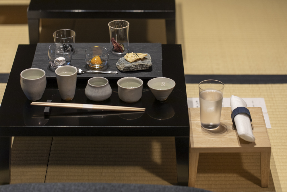 「長谷川栄雅 六本木」の日本酒体験の様子。脚付き膳に供される「長谷川栄雅」の日本酒5種類と小林シェフ創作のアテが並ぶ。