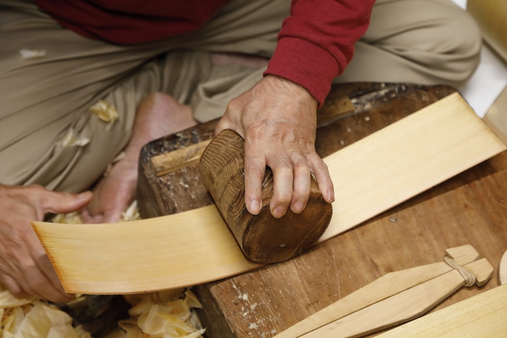 曲物師は水につけた能登ヒバを鉋で削り、型に沿って曲げる